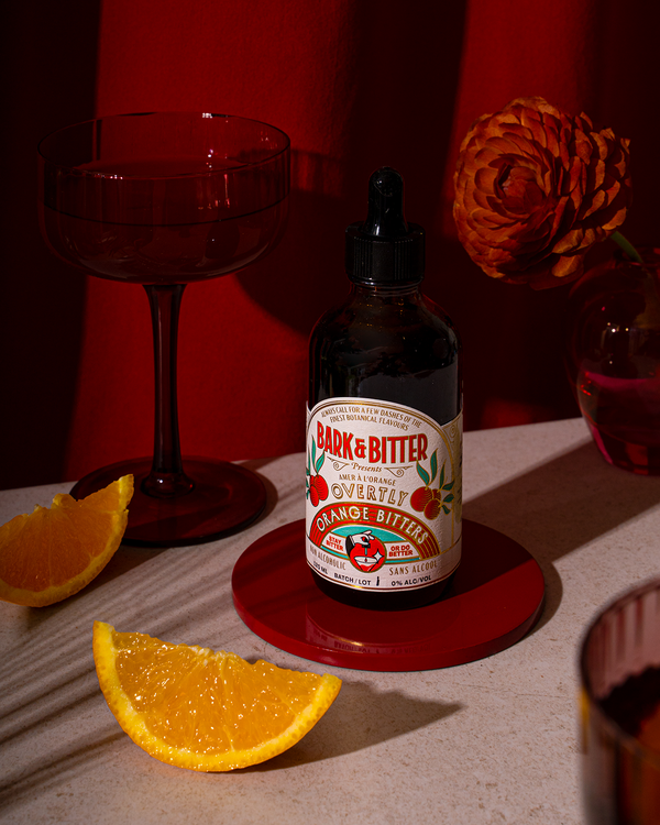 Overtly Orange non-alcoholic bitters on a red coaster beside orange wedges