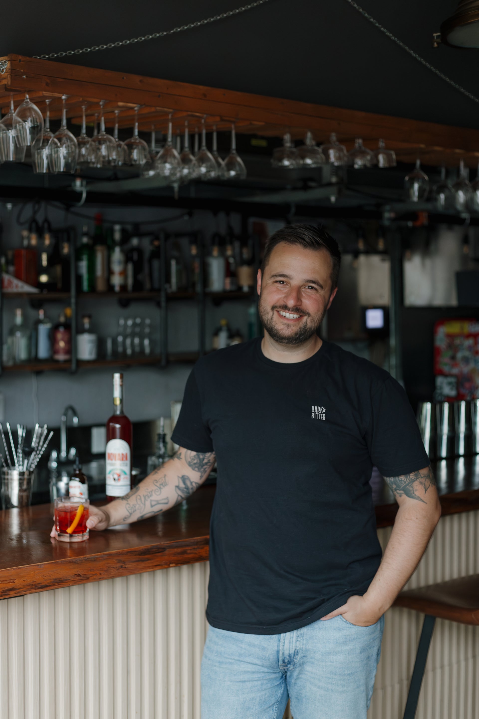 Bark & Bitter founder Nick Nemeth behind a bar, holding a non-alcoholic Negroni made with Novara Aperitivo